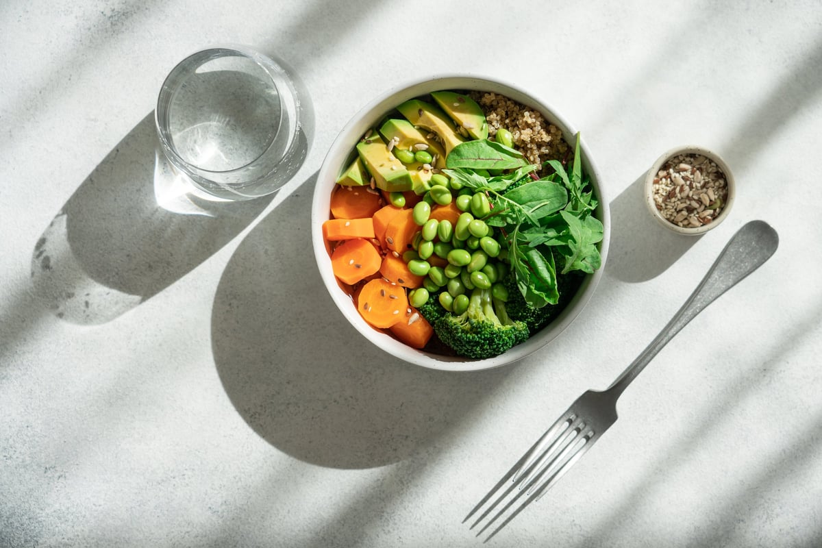 White Bowl with Healthy Quinoa Salad, Edamame Beans, Broccoli, Carrot, Lettuce Leaves and Avocado on White Background with Shadows